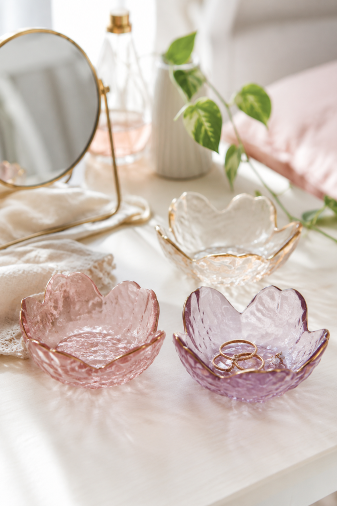 Three petal-shaped glass trinket bowls with gold rims holding rings and earrings